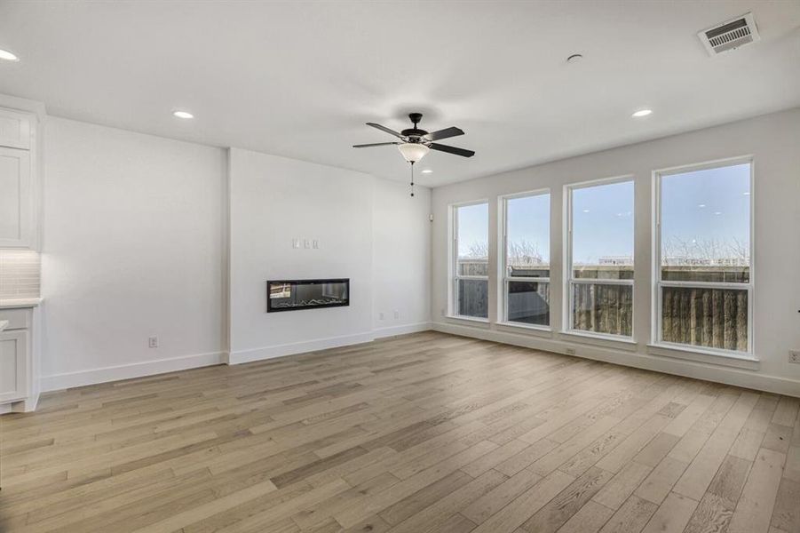 Unfurnished living room with ceiling fan, light wood-type flooring, a glass covered fireplace, and recessed lighting