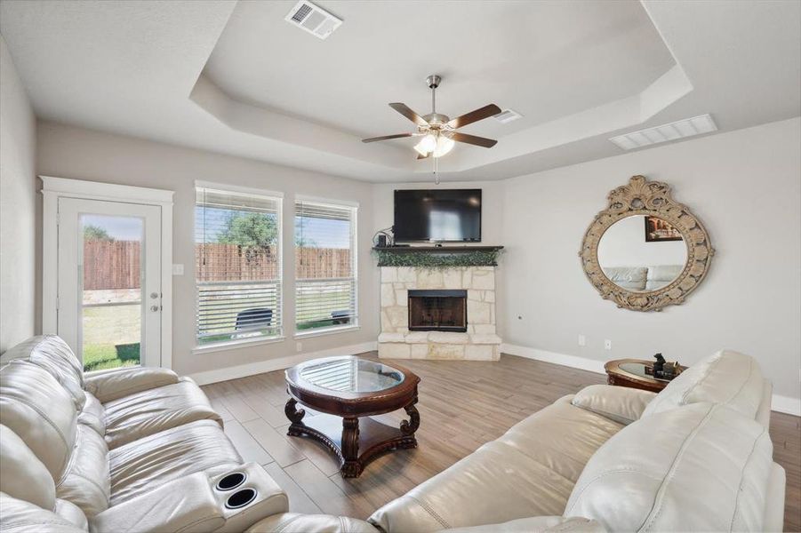 Living room featuring ceiling fan, a stone fireplace, a raised ceiling, and hardwood / wood-style floors