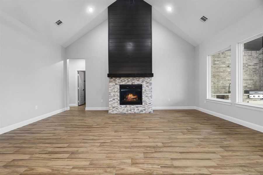 Unfurnished living room featuring a stone fireplace, light wood-type flooring, and high vaulted ceiling