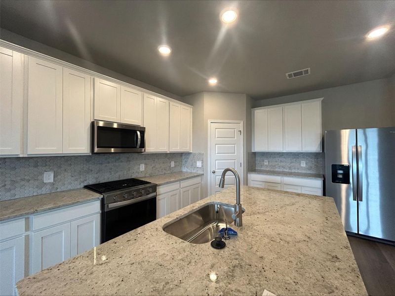 Kitchen with appliances with stainless steel finishes, white cabinets, backsplash, dark wood-type flooring, and recessed lighting Kitchen with appliances with stainless steel finishes, white cabinets, backsplash, dark wood-type flooring, and recessed lighting