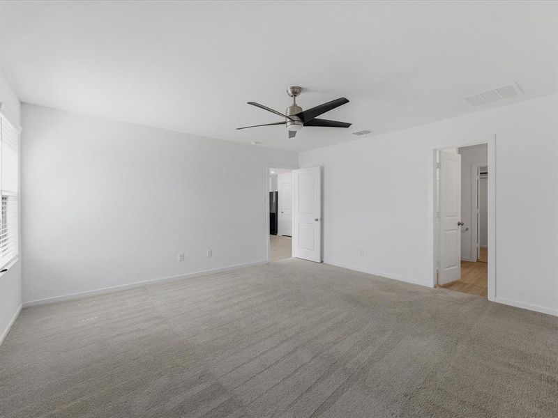 Spacious room featuring neutral carpeting, white walls, a ceiling fan with integrated lighting, and multiple doorways
