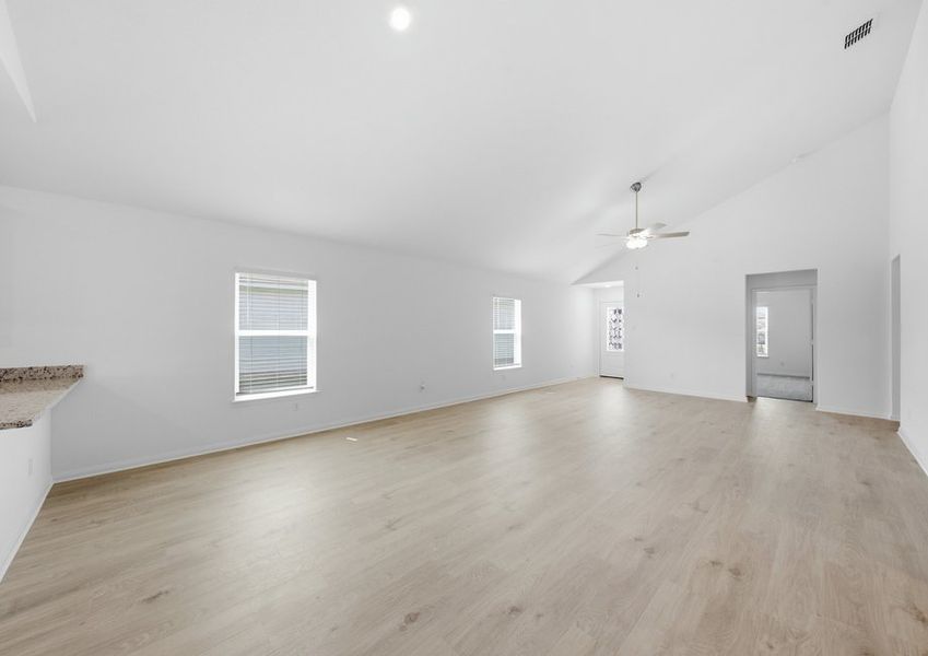 Wide view of the family room featuring a ceiling fan and wood-look vinyl flooring open to the kitchen. Wide view of the family room featuring a ceiling fan and wood-look vinyl flooring open to the kitchen.