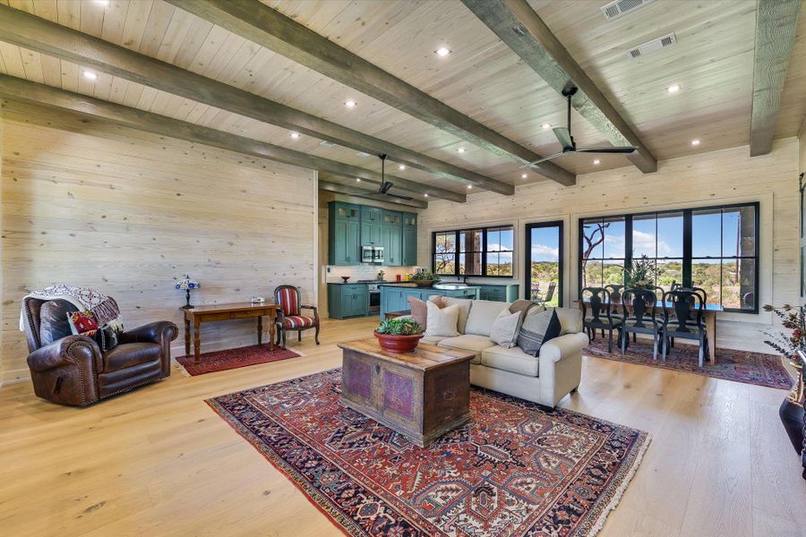 Living area featuring wood walls, light wood-style flooring, ceiling fan, a wooden ceiling with exposed beams, and recessed lighting