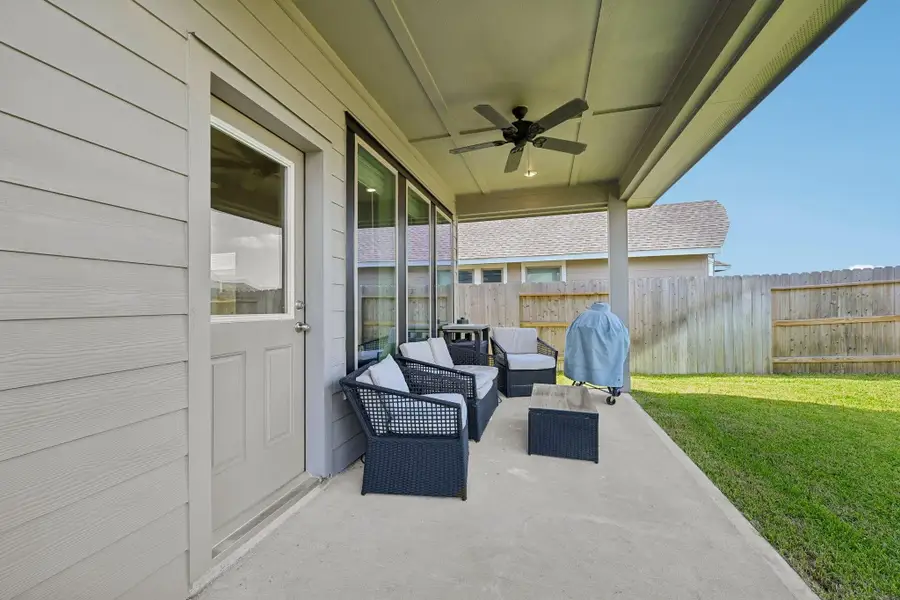 Charming covered patio with cozy seating, ceiling fan, and a view of the fenced-in backyard—perfect for outdoor relaxation and entertaining.