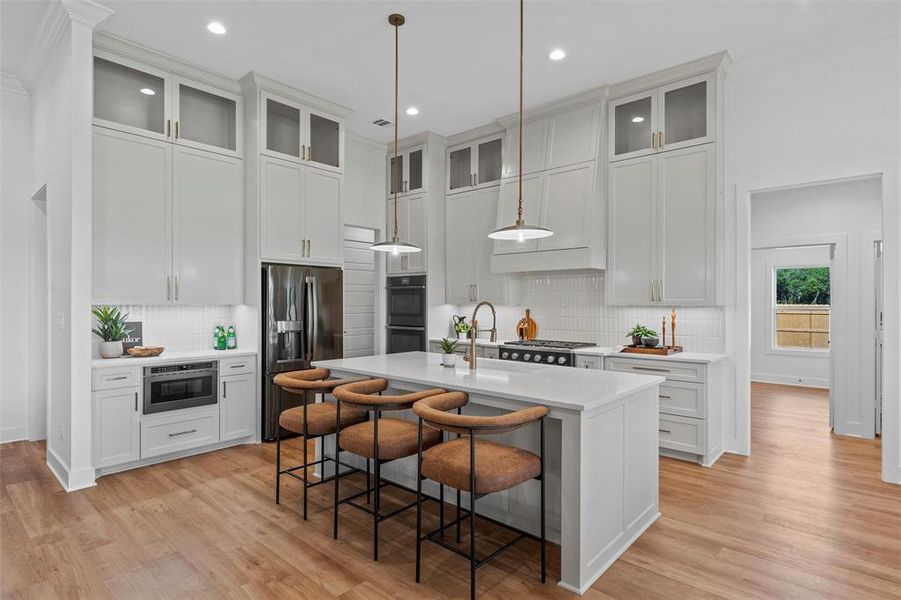 Kitchen with stainless steel appliances, light countertops, tasteful backsplash, a breakfast bar, and an island with sink