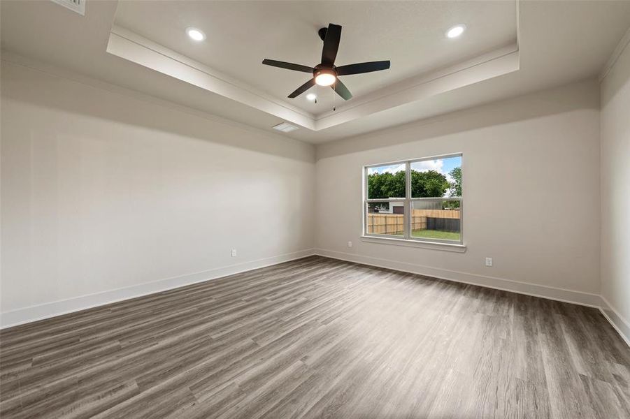 Spacious room featuring wood-finish flooring, a tray ceiling, recessed lighting, and a modern ceiling fan Spacious room featuring wood-finish flooring, a tray ceiling, recessed lighting, and a modern ceiling fan