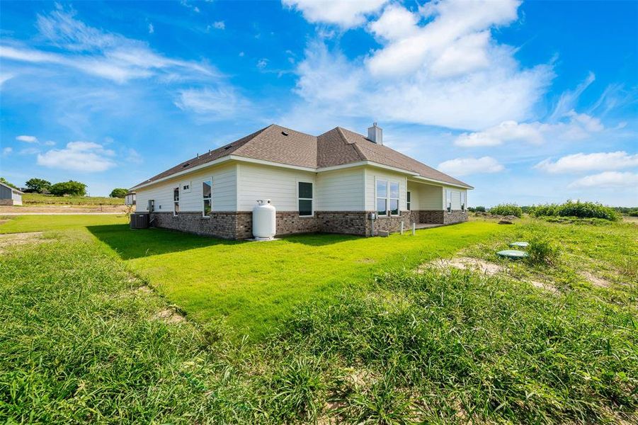 View of home's exterior with brick siding, a yard, a chimney, and roof with shingles