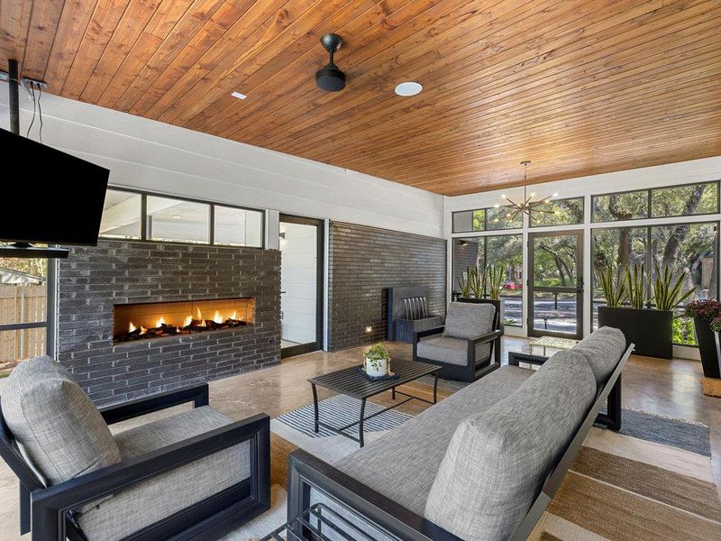 Living area with plenty of natural light, a brick fireplace, expansive windows, concrete floors, and wood ceiling