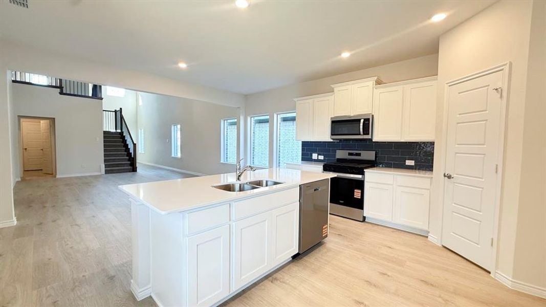 Kitchen featuring white cabinets, appliances with stainless steel finishes, decorative backsplash, open floor plan, and a kitchen island with sink