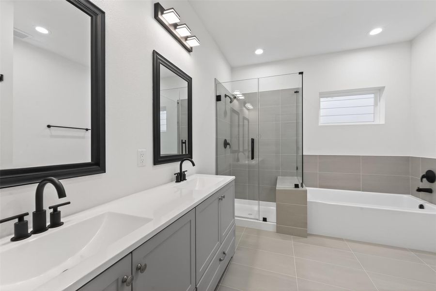 This modern bathroom features a dual-sink vanity with sleek black fixtures, a spacious glass-enclosed shower, and a separate bathtub. The neutral tile flooring and walls create a clean and elegant look.