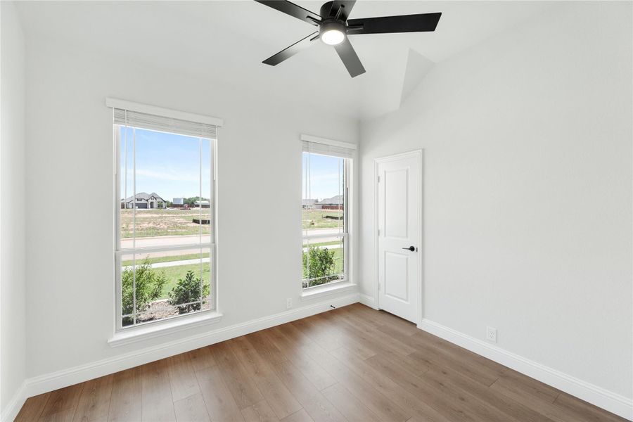 Empty bedroom with vaulted ceiling, black ceiling fan, hardwood floors, and two windows with neighborhood views