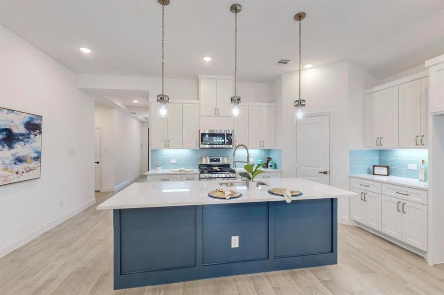 Kitchen featuring backsplash, stainless steel appliances, an island with sink, and light hardwood / wood-style flooring