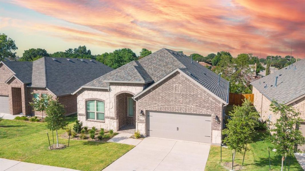 French provincial home featuring stone siding, brick siding, a front yard, and concrete driveway
