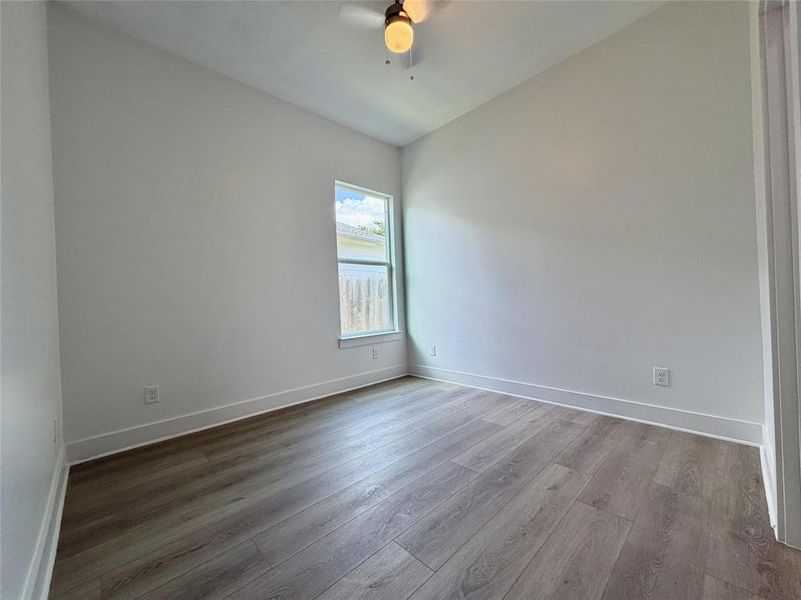 Room featuring wood-finish flooring, a ceiling fan with integrated lighting, and a single window offering exterior views Room featuring wood-finish flooring, a ceiling fan with integrated lighting, and a single window offering exterior views