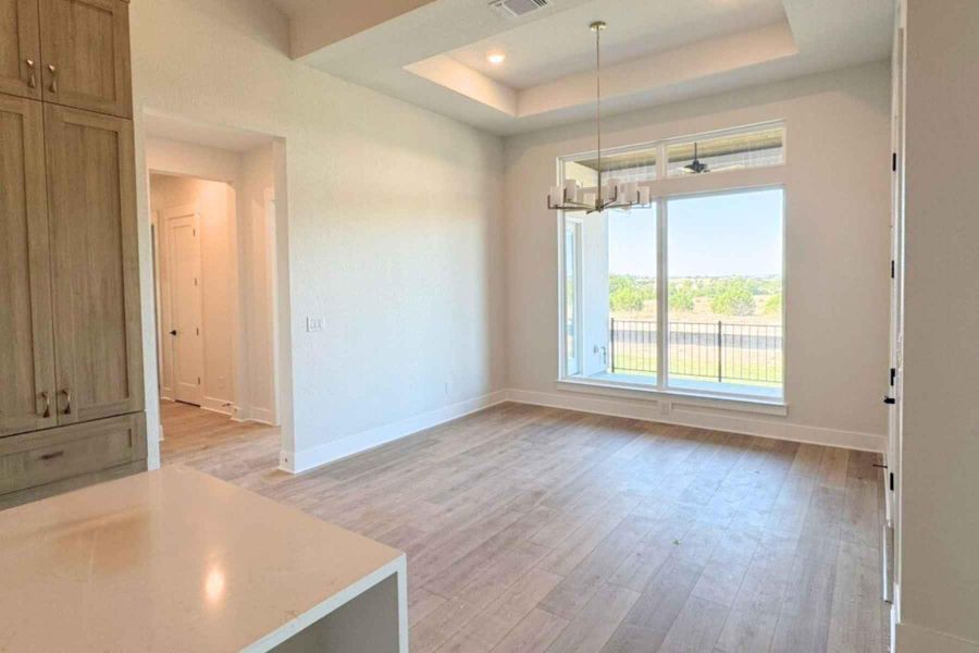 Unfurnished dining area featuring a chandelier, a raised ceiling, light wood finished floors, and recessed lighting