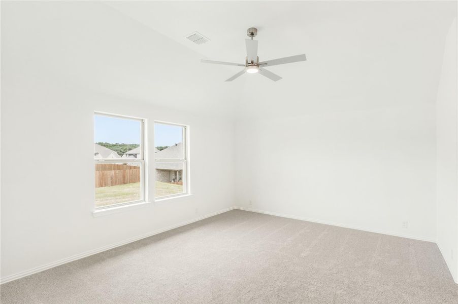 Empty bedroom with carpet flooring, ceiling fan, and two windows overlooking backyard