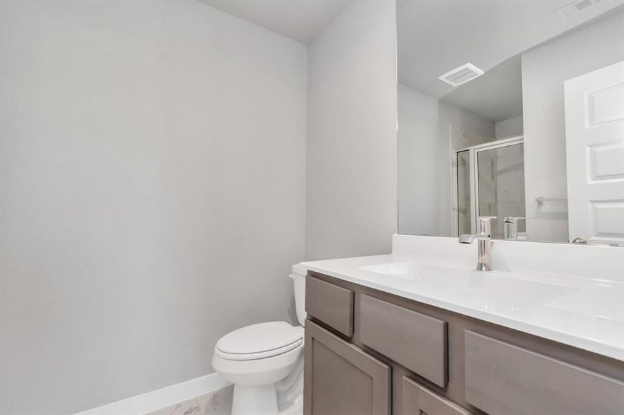 Guest suite bathroom, where tile flooring complements a walk-in shower with tile surround. Dark wood cabinets complete with a beautiful light countertop, enhances the space for a truly inviting ambiance.  Sample photo of completed plan. As-built color and selections may vary.