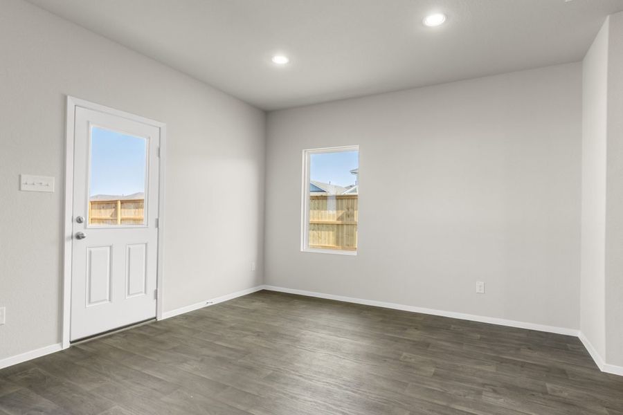 Image of a dining room area with dark vinyl flooring, cream walls, a window and a white back door