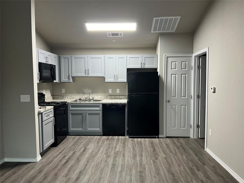 Kitchen featuring black appliances, wood finished floors, a sink, and light countertops