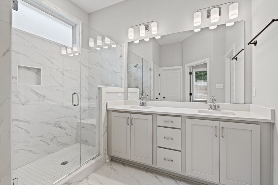 Full bathroom with plenty of natural light, a marble finish shower, light marble finish flooring, and double vanity