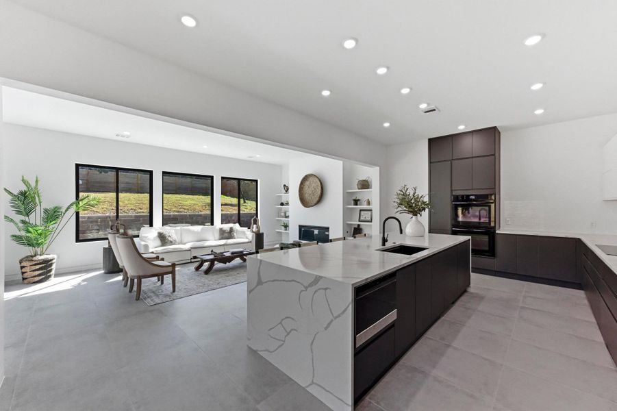 Kitchen with modern cabinets, a glass covered fireplace, a center island with sink, recessed lighting, and light stone countertops