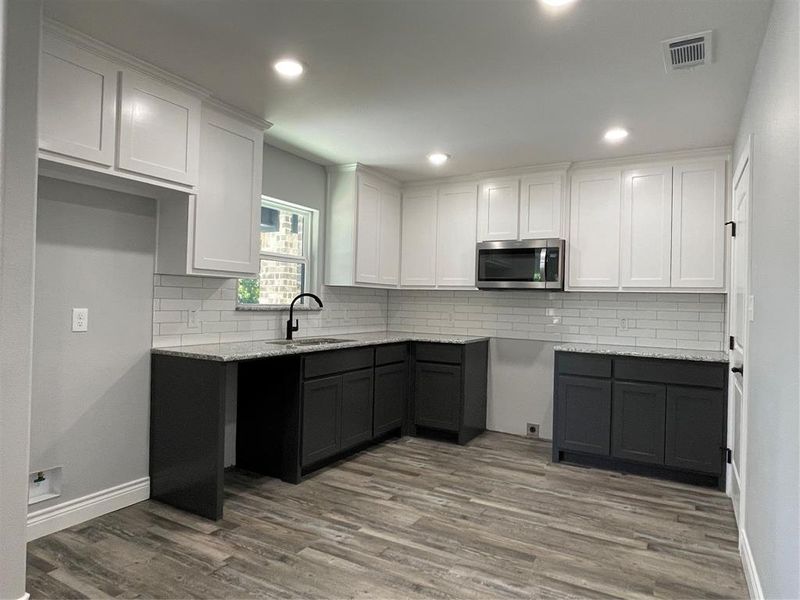 Kitchen with light stone counters, sink, light hardwood / wood-style flooring, white cabinetry, and decorative backsplash