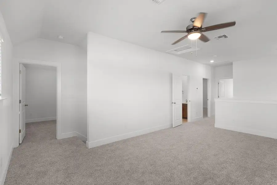 A spacious carpeted room with a vaulted ceiling and a ceiling fan offers ample space.