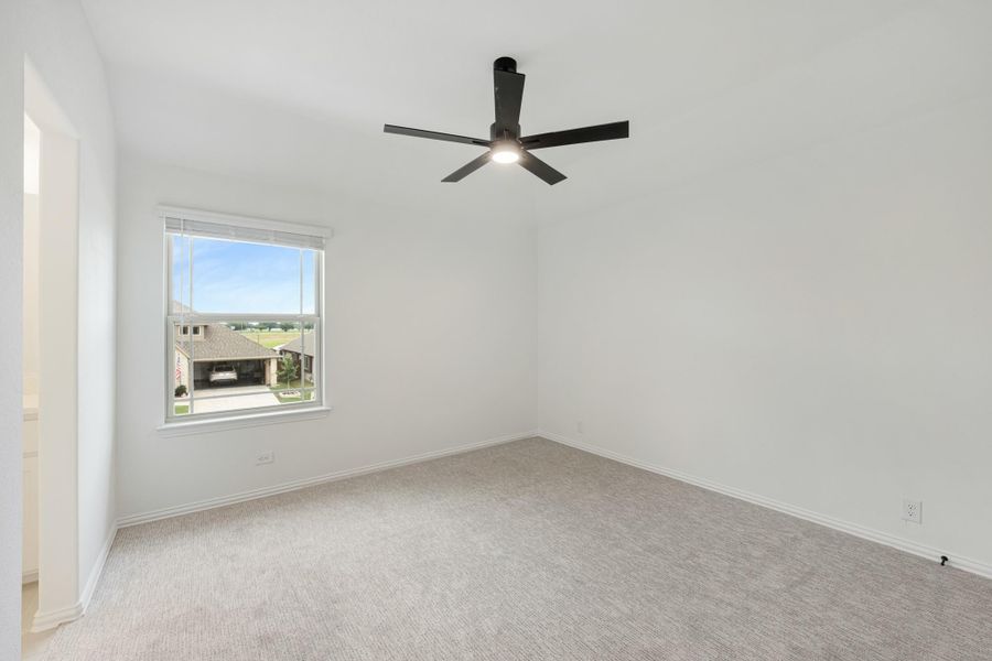 Empty bedroom with white walls, gray carpet, black ceiling fan, and a window with neighborhood view Empty bedroom with white walls, gray carpet, black ceiling fan, and a window with neighborhood view