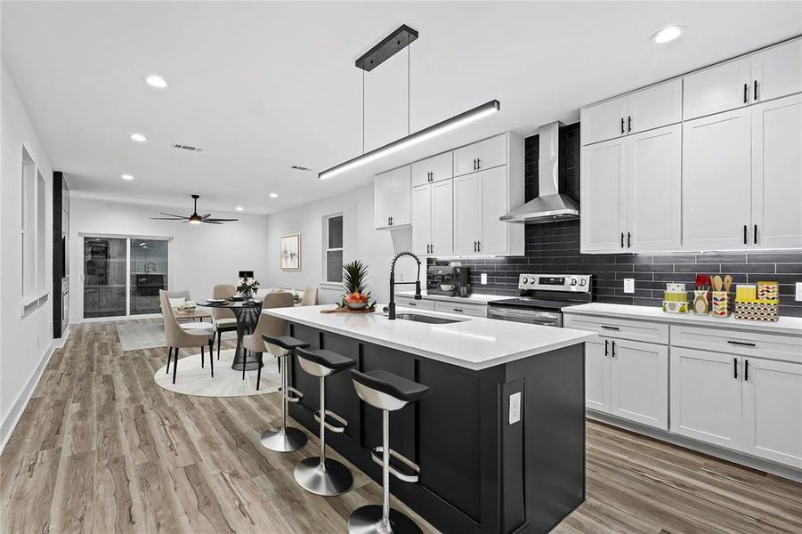 Kitchen featuring wall chimney range hood, decorative light fixtures, white cabinets, stainless steel range with electric cooktop, and an island with sink