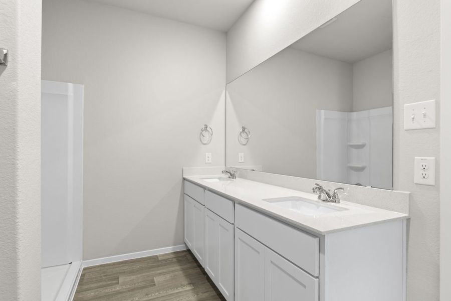 Image of a bathroom with cream walls, a white jack and jill vanity, a large mirror and a standing shower