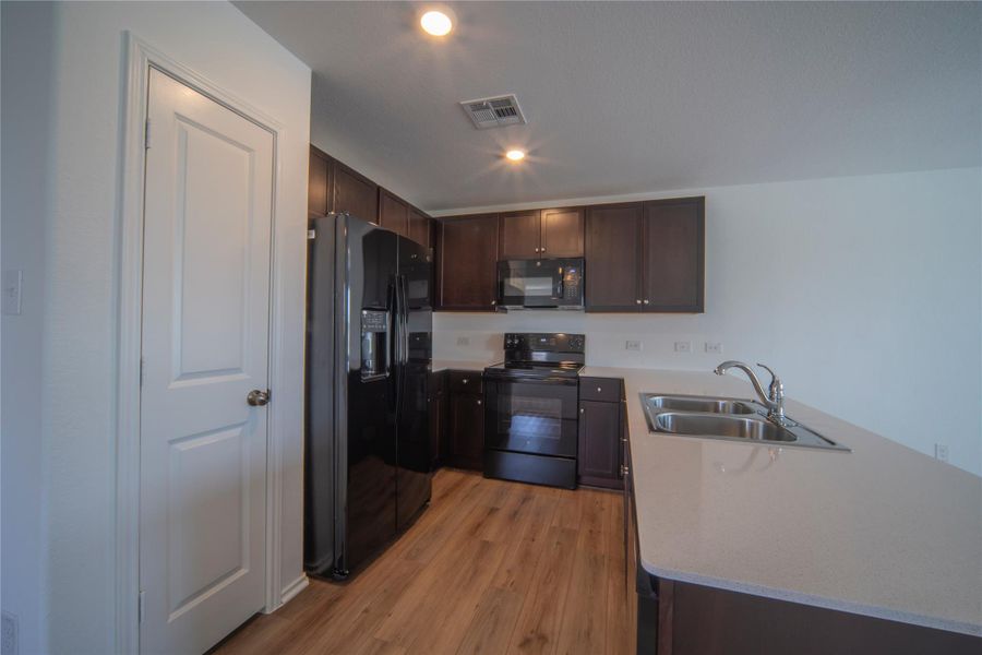 Kitchen featuring dark brown cabinetry, black appliances, a peninsula, light wood-style floors, and recessed lighting