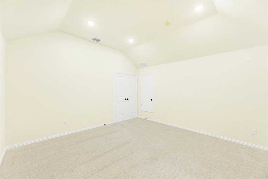Empty bedroom with vaulted ceiling, carpet flooring, and two white doors Empty bedroom with vaulted ceiling, carpet flooring, and two white doors