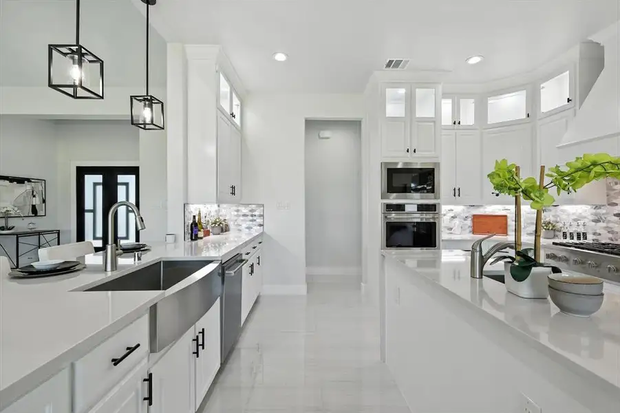 Kitchen with decorative light fixtures, backsplash, appliances with stainless steel finishes, white cabinetry, and range hood Kitchen with decorative light fixtures, backsplash, appliances with stainless steel finishes, white cabinetry, and range hood