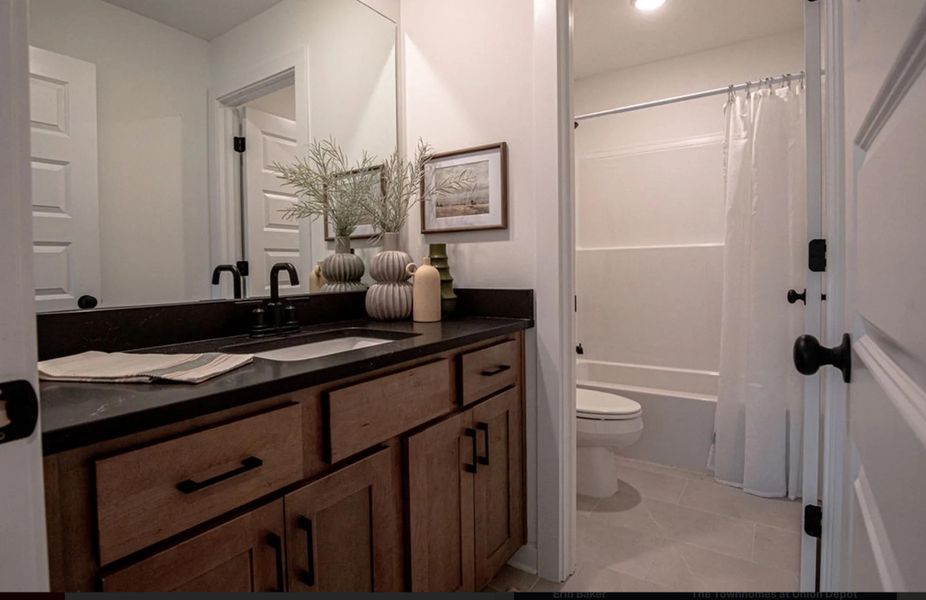 Bathroom featuring a wood-finish vanity with dark countertop, integrated sink, and matte black fixtures