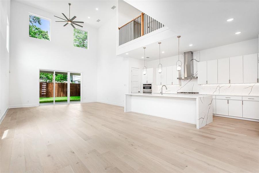 Unfurnished living room with plenty of natural light, light wood-type flooring, a ceiling fan, a towering ceiling, and recessed lighting