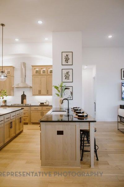 Kitchen with wall chimney exhaust hood, light brown cabinets, a kitchen breakfast bar, light wood-type flooring, and pendant lighting Kitchen with wall chimney exhaust hood, light brown cabinets, a kitchen breakfast bar, light wood-type flooring, and pendant lighting