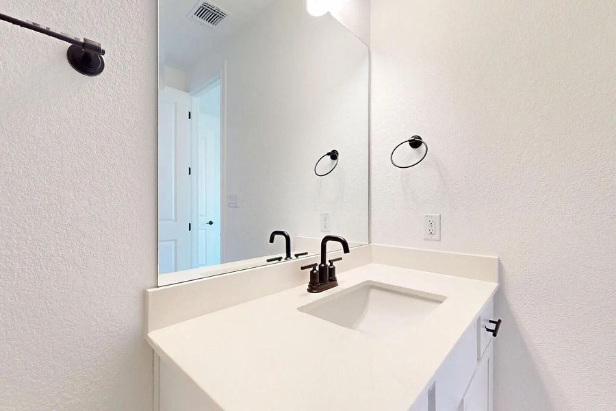 The bathroom features a vanity with a white countertop and a rectangular sink, complemented by a black faucet and a wall-mounted mirror