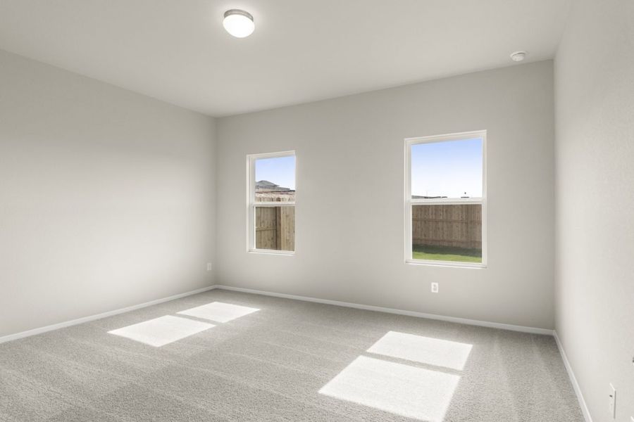 Image of a primary bedroom with tan carpeting, light grey walls and two windows