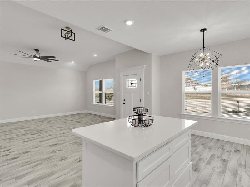 Kitchen with white cabinetry, decorative light fixtures, a kitchen island, ceiling fan with notable chandelier, and light wood-type flooring