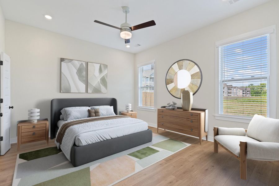 Bright bedroom featuring wood-finish flooring, two window openings, and a ceiling fan with integrated lighting Bright bedroom featuring wood-finish flooring, two window openings, and a ceiling fan with integrated lighting
