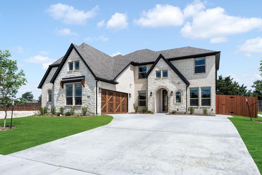Two-story home with light stone exterior, wood garage doors, and wide concrete driveway