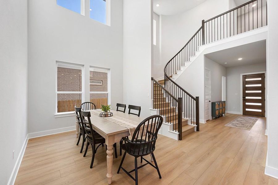 Towering ceilings and light wood floors create an airy dining space beside a sweeping staircase.