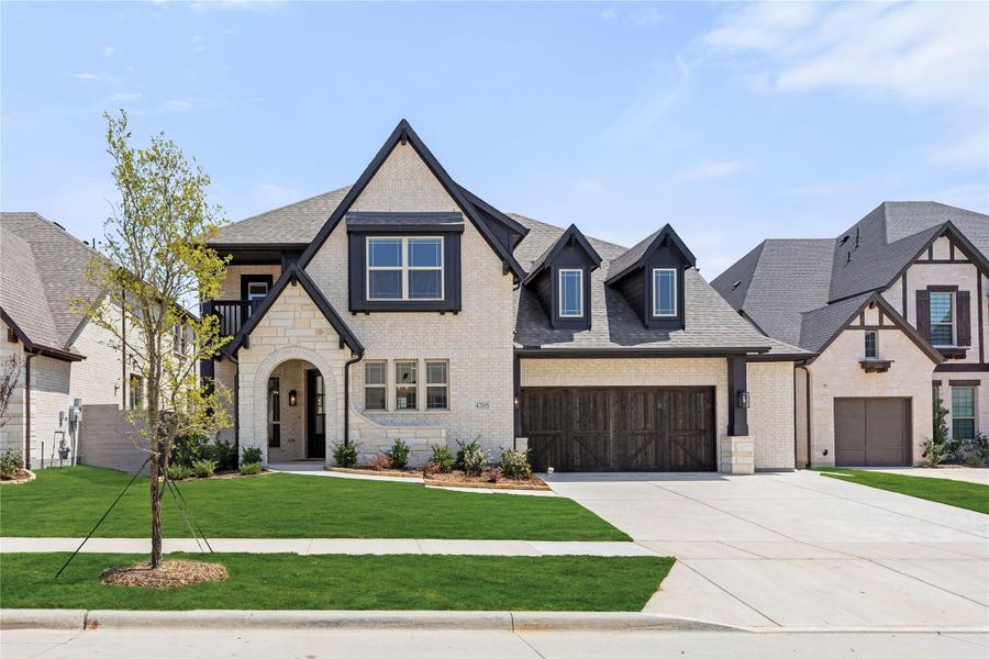 Two-story home with cream brick exterior, dark trim, arched entry, and two-car garage with wood doors Two-story home with cream brick exterior, dark trim, arched entry, and two-car garage with wood doors