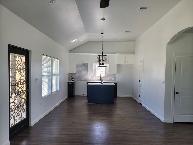Kitchen with dual tone cabinetry, pendant lighting, backsplash, dark wood-type flooring, and an island with sink