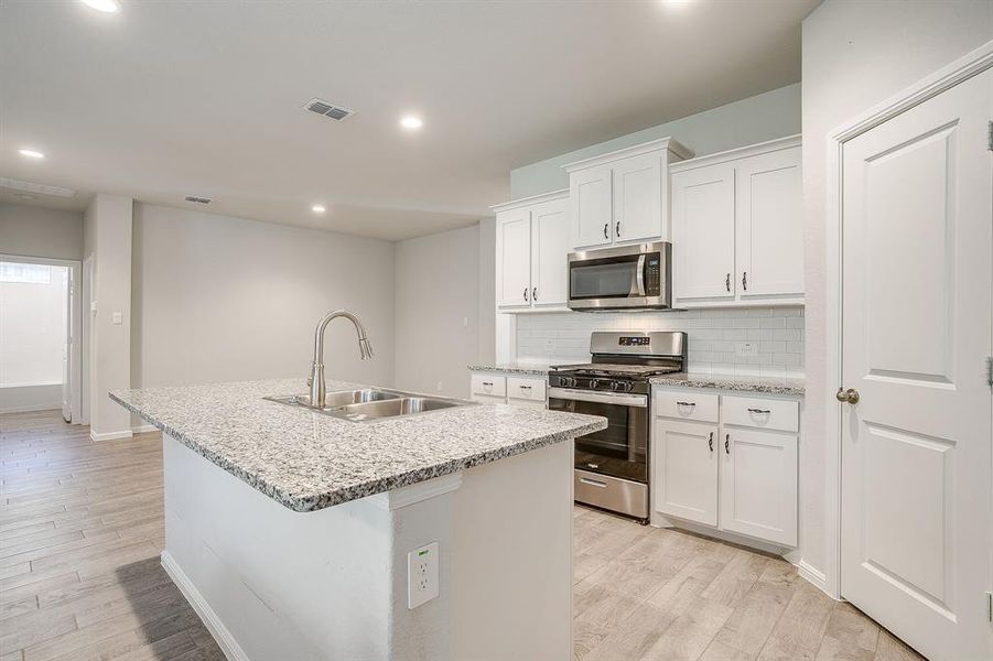 Kitchen with stainless steel appliances, decorative backsplash, white cabinets, light wood-style floors, and recessed lighting