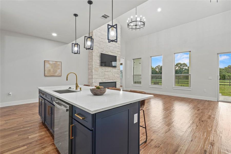 Kitchen with high vaulted ceiling, open floor plan, light wood-style floors, a stone fireplace, and a center island with sink Kitchen with high vaulted ceiling, open floor plan, light wood-style floors, a stone fireplace, and a center island with sink