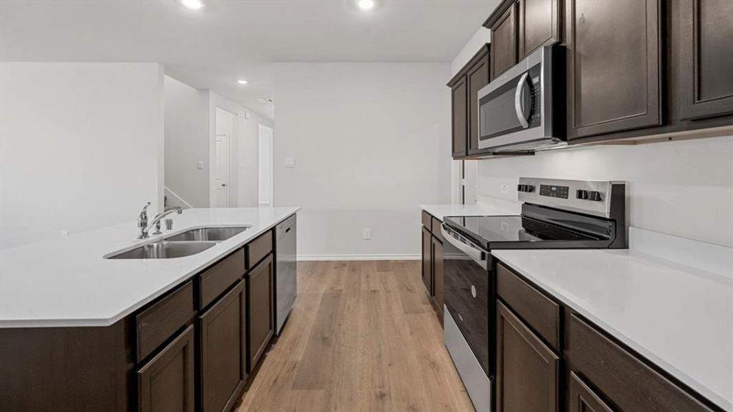 Kitchen featuring appliances with stainless steel finishes, dark brown cabinets, light wood-type flooring, a center island with sink, and recessed lighting