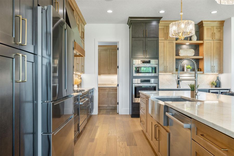 Kitchen featuring light stone counters, light wood-style floors, appliances with stainless steel finishes, decorative light fixtures, and recessed lighting