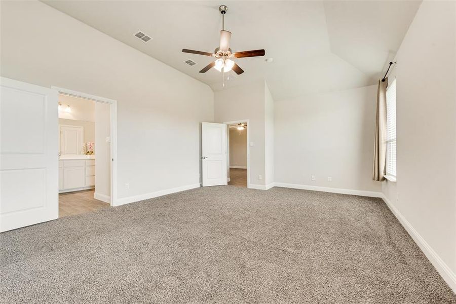 Unfurnished bedroom featuring light carpet, ceiling fan, lofted ceiling, and ensuite bathroom