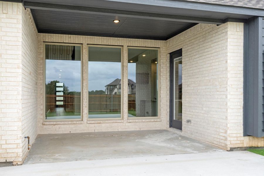 Covered back patio with concrete slab, large windows, and dark entry door on light brick exterior Covered back patio with concrete slab, large windows, and dark entry door on light brick exterior